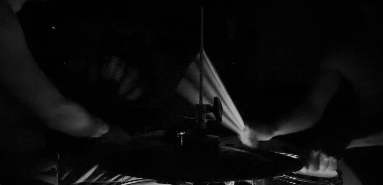 Hands and sticks in motion over hi-hat and drums, live in the dark